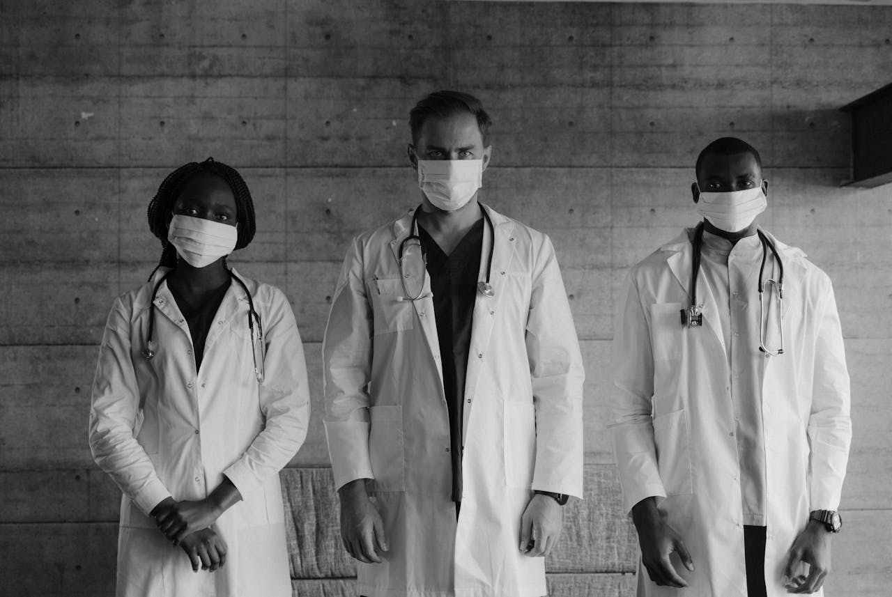 Black and white photo of three healthcare workers wearing masks and stethoscopes indoors.